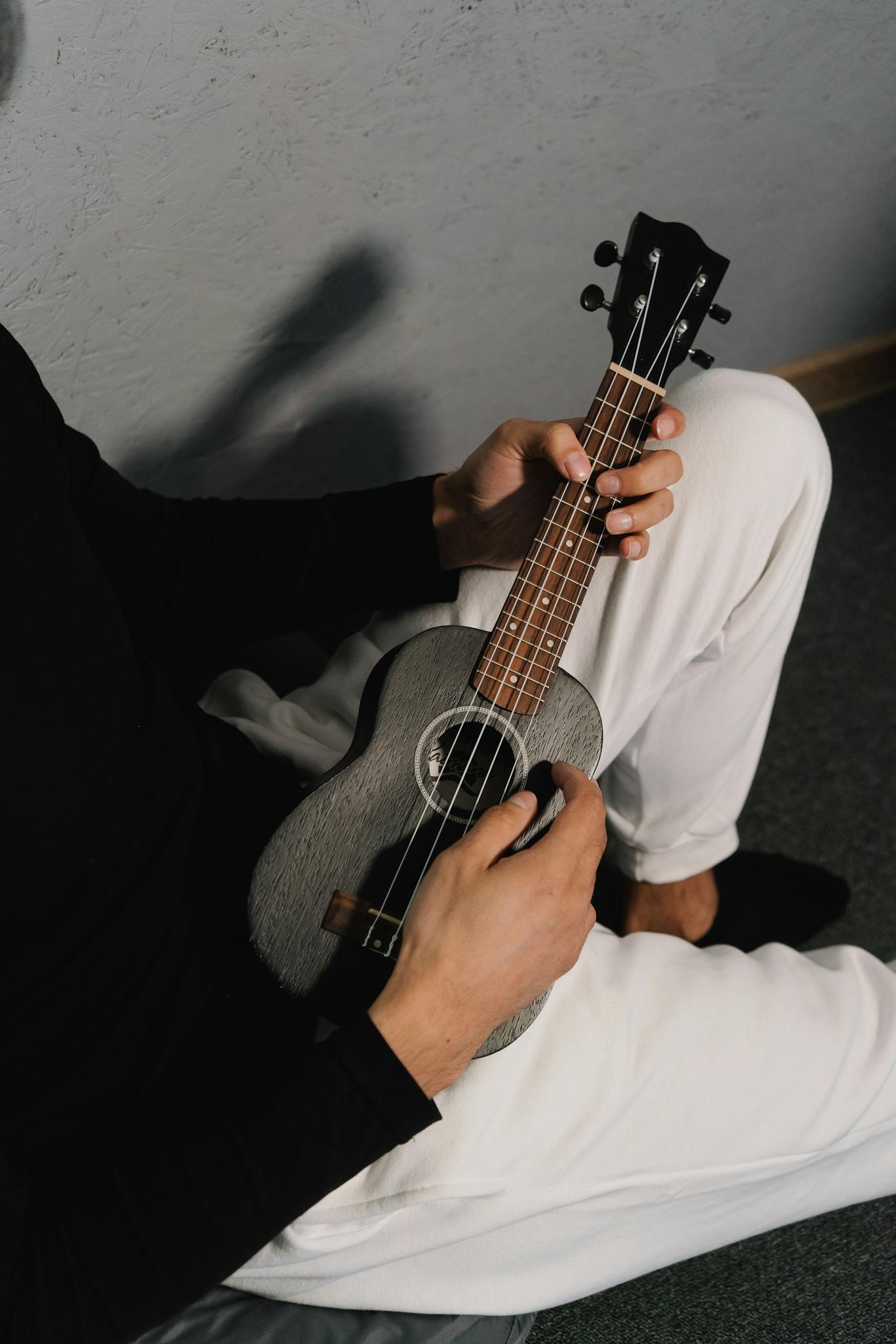 Close-up of a person playing a ukulele indoors, wearing black and white attire.